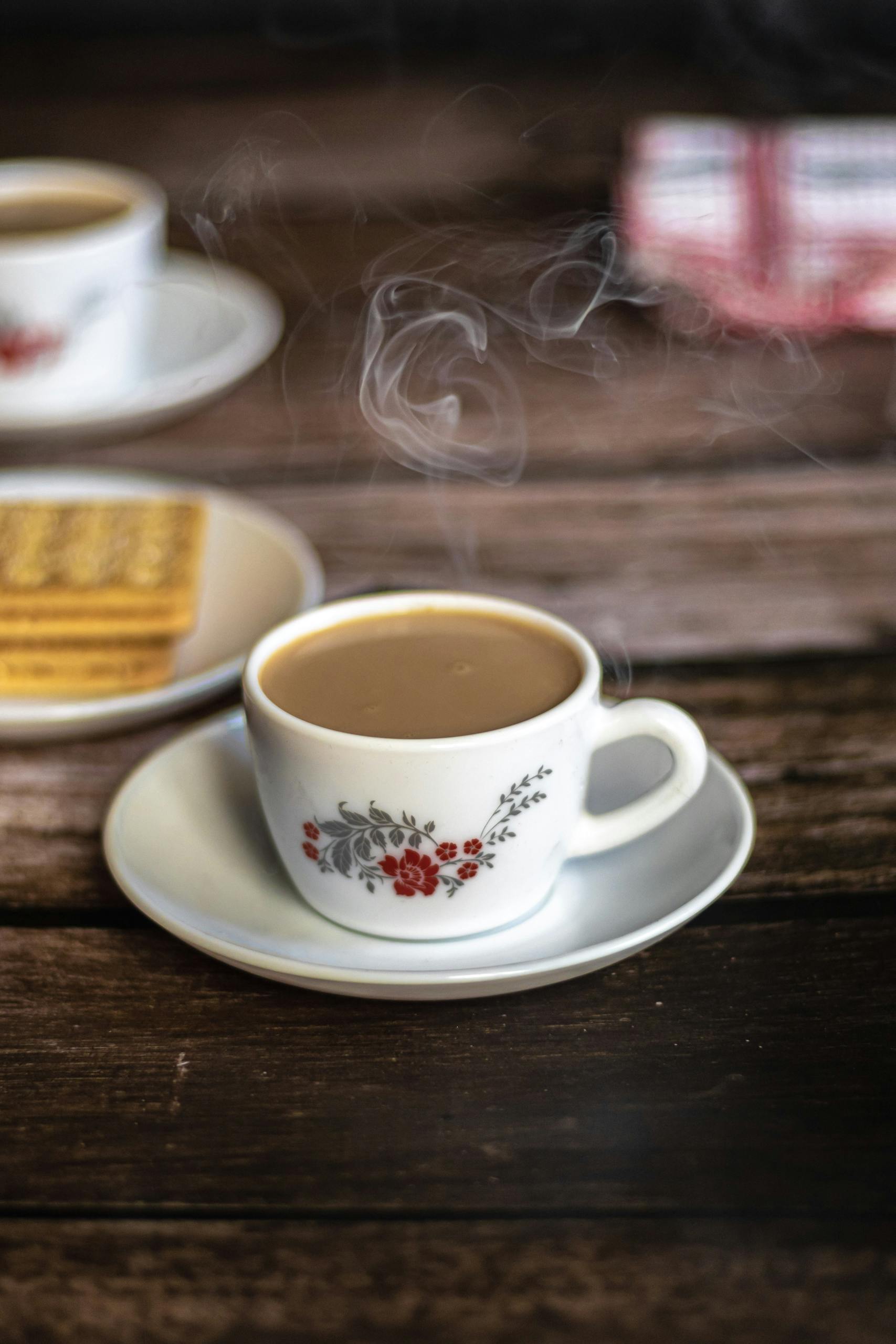 A cozy close-up of a steaming cup of tea with biscuits on a rustic wooden table.